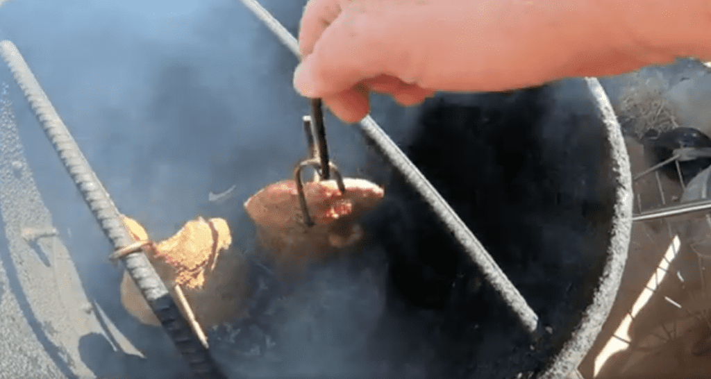 Flank steaks hanging in a pit barrel cooker over charcoaol.